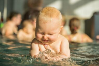 lachenden Baby mit zugekniffenen Augen wird von Händen im Wasser gehalten