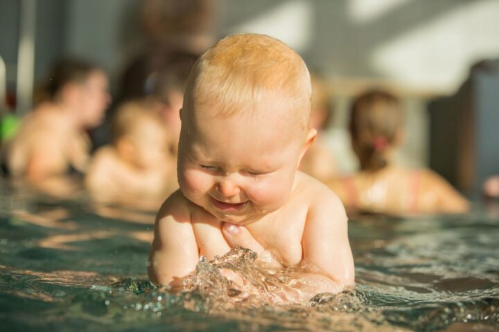 lachenden Baby mit zugekniffenen Augen wird von Händen im Wasser gehalten
